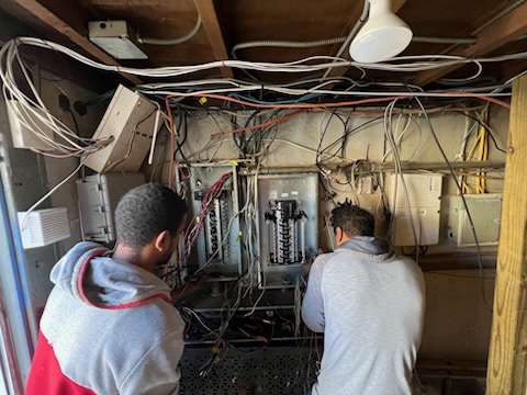 Two Electric Power Pro electricians tracing circuits at an open panel bank to find a fault