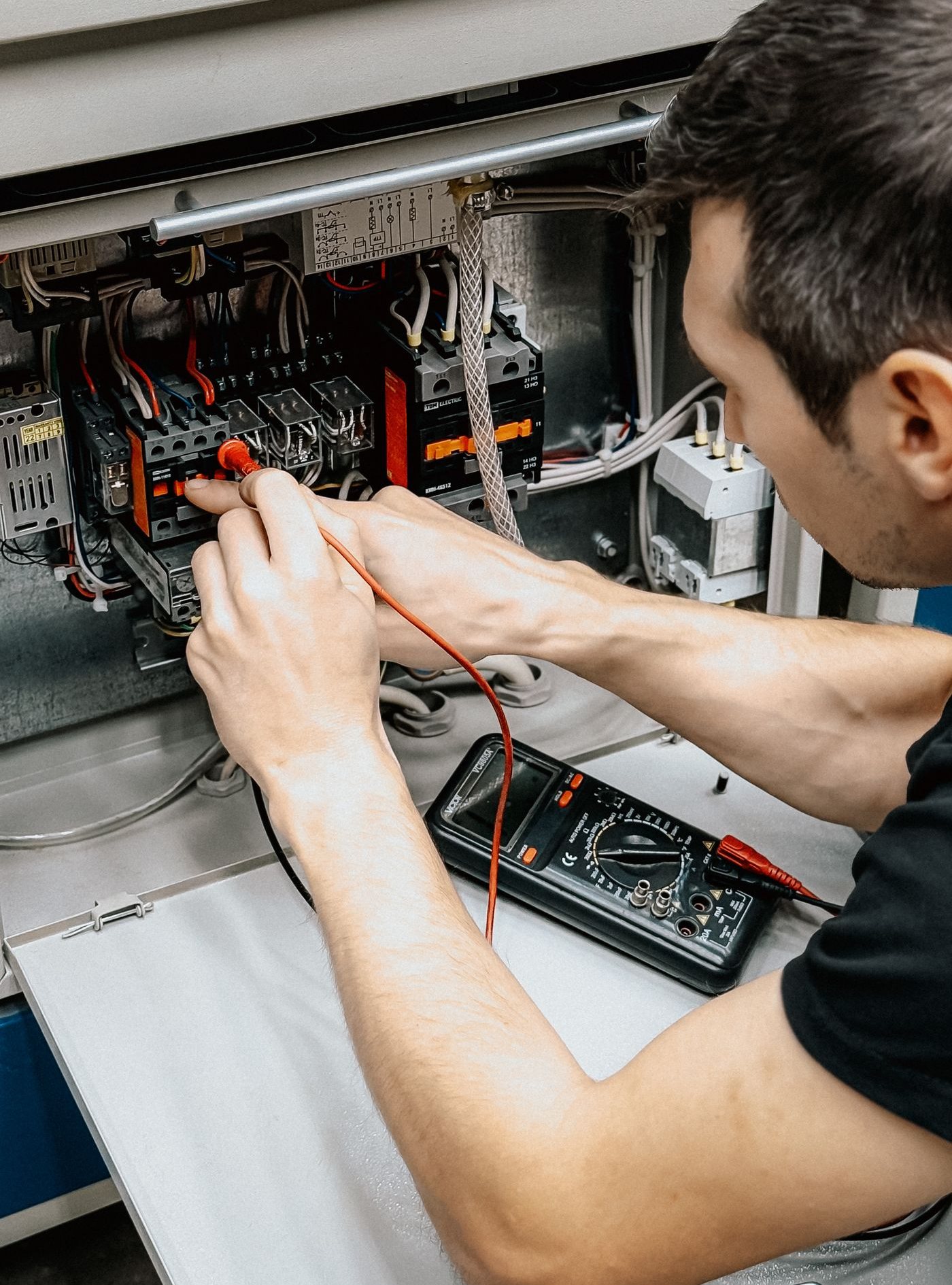 Electrician testing an open electrical panel with a multimeter